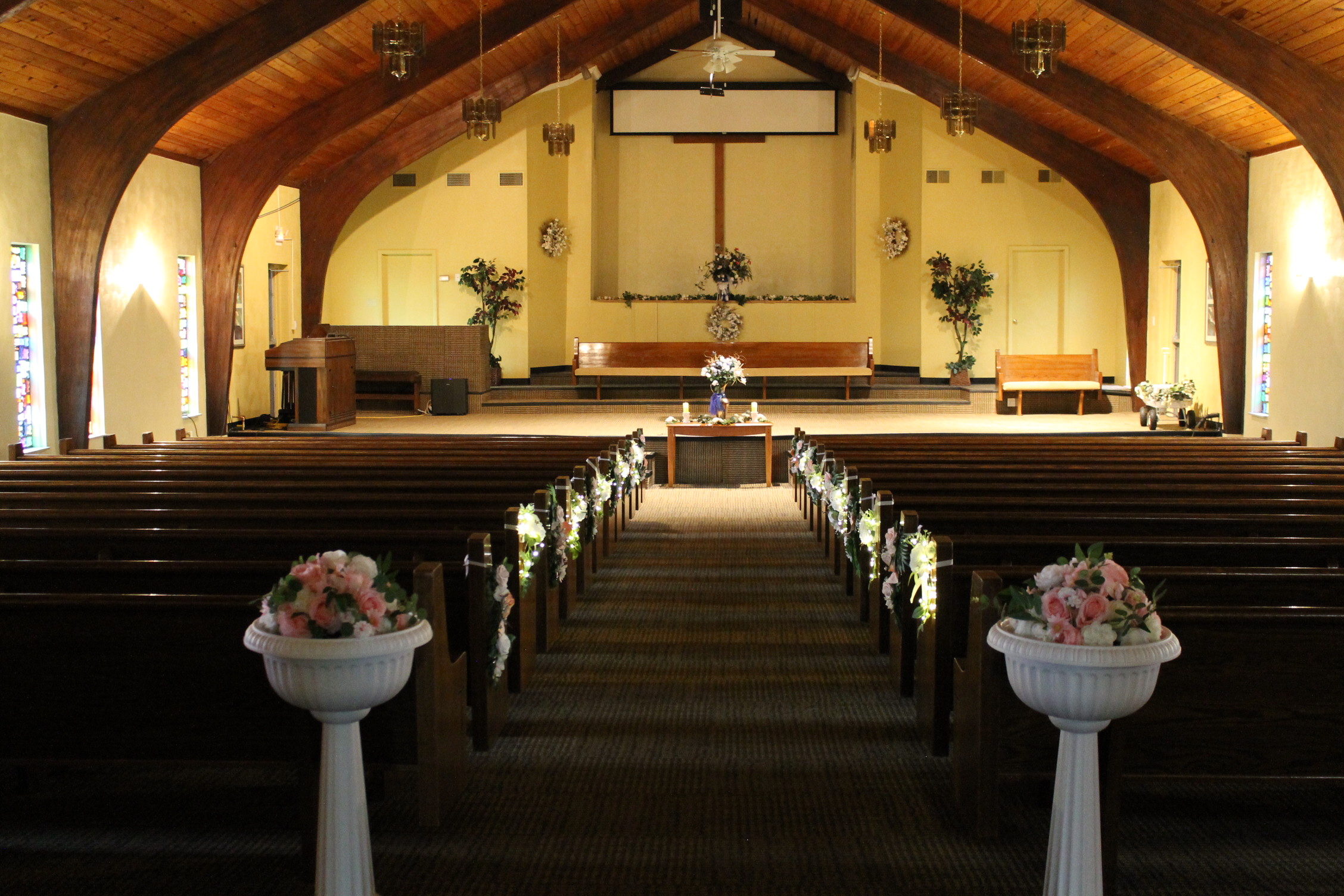 Interior of Chapel on the Lane in Dayton, Ohio, decorated for a wedding with floral arrangements along the aisle and a cross above the altar.