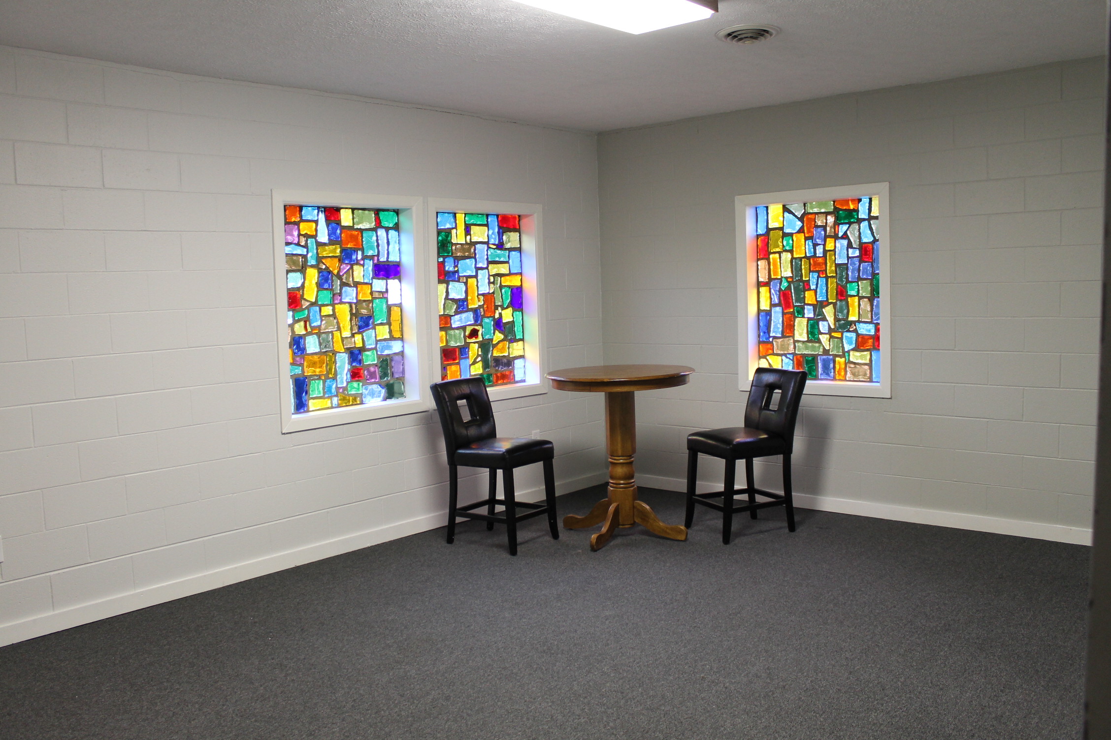 Flexible party room at Chapel on the Lane in Dayton, Ohio, featuring stained glass windows, a high-top table, and two chairs in a private corner setting.
